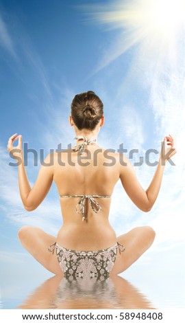 Young attractive brunette woman in swim suit doing yoga moves or meditating over sky