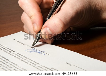 Close up of the hand holding the pen and signing the contract