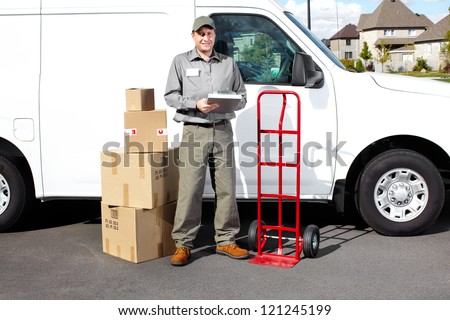 Smiling delivery courier standing near the white truck. Shipping service.