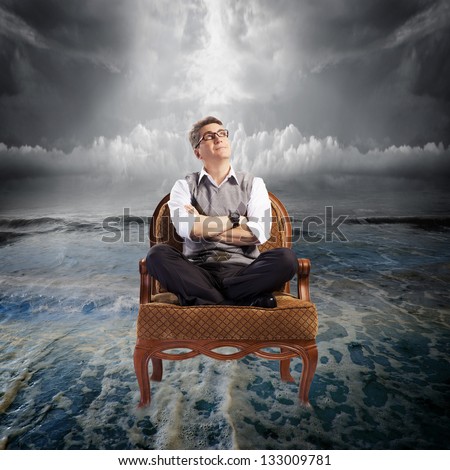 Man sitting on armchair in the ocean water. Danger concept.