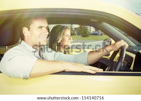 Two young smiling people in a yellow car