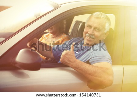 Two Happy Smiling Elderly People In Car Pointing Thumb