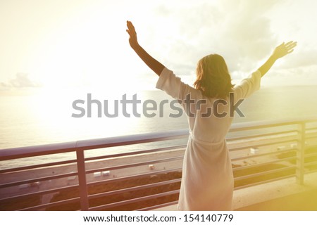 Happy woman with hands up to sky looking at ocean