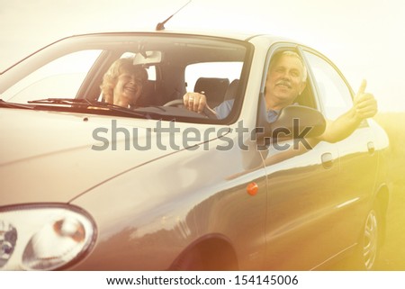 Two Happy Smiling Elderly People In Car Pointing Thumb