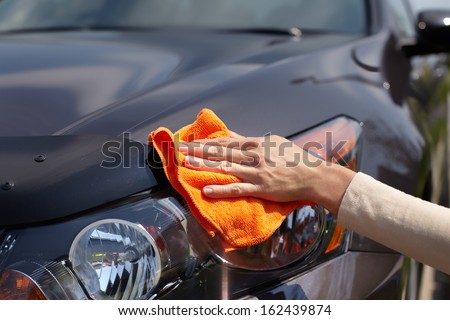 Hand with microfiber cloth cleaning car.