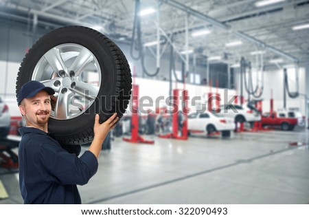 Smiling repairman with tire a in car repair service.