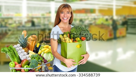 Woman with paper bag of vegetables over grocery store background.