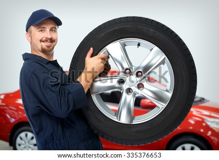 Smiling car mechanic with a tire over red car background.