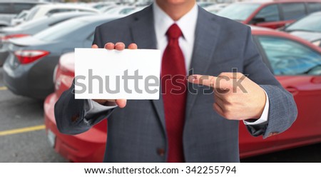 Auto dealer with a business card over vehicles background.