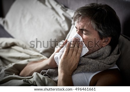 Sick man with cold lying in bed and blow nose.