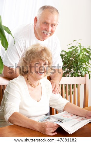 Happy smiling elderly couple reading a magazine  at home