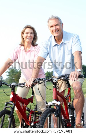 Happy elderly senior couple biking in park