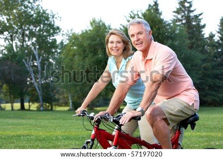 Happy elderly senior couple biking in park