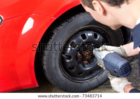 Mechanic changing wheel on car with impact wrench.
