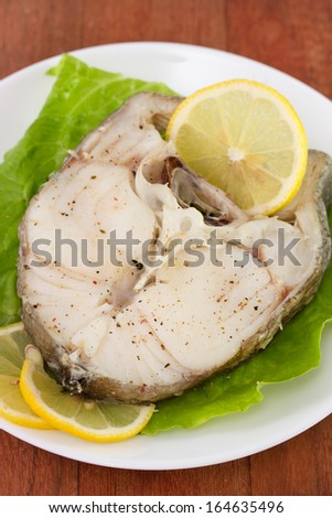 boiled fish with lemon and lettuce on plate