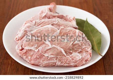 frozen pork with bay leaf on white plate on brown wooden background