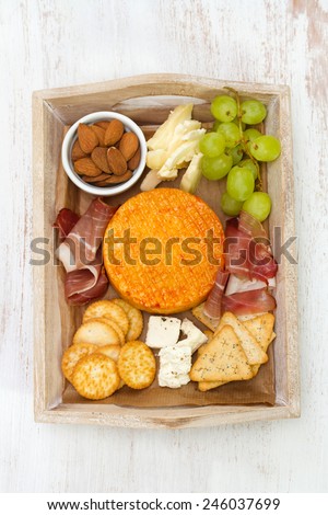 cheese with meat, grape and nuts on tray on white wooden background