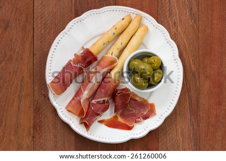 prosciutto with olives on white plate on brown background