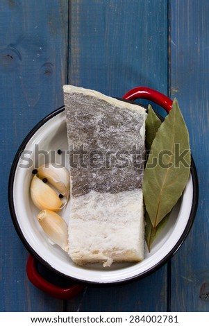 codfish with garlic and bay leaf in dish on blue wooden background