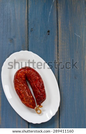 smoked sausage on dish on white dish on blue wooden background