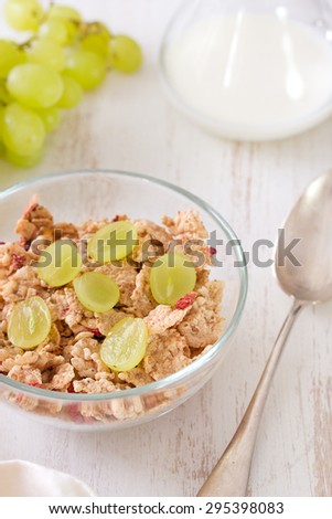 cereals with grapes on bowl with milk and spoon on white wooden background