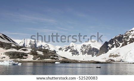 Small bay in Antrarctic peninsula. People on the shore and rubber boat is passing by