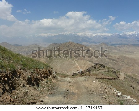Dirt path through the mountains around Kabul, Afghanistan leading to snow-capped Hindu Kush in the distance