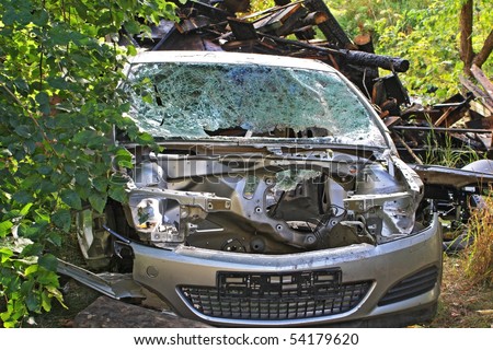 A sight of a car broken in a car crash with scorched ruins on the background