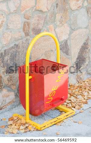 A red garbage bin with the stone wall on the background