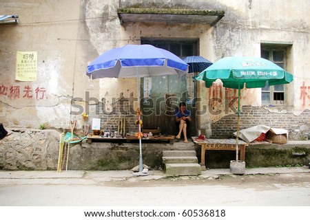 YANGSHUO, CHINA - MAY 18: A hawker sits along the street in an old village in the afternoon on 18 May, 2010 in Yangshuo. He sells different goods for the villagers.