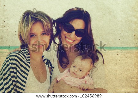 two beautiful girls with a baby on the beach. Photo in old color image style.