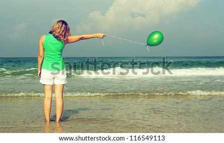 Beautiful girl with green balloon on the beach. Old style colors.