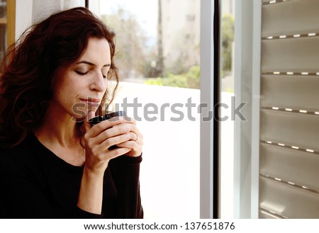 Photo of a beautiful young female drinking coffee and looking out the window