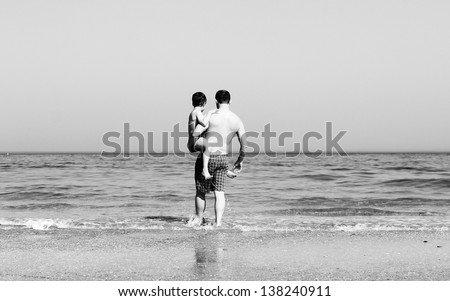 father and son going to swim in the sea. black and white photo.
