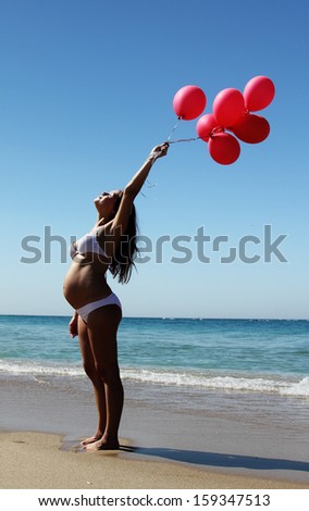 Young pregnant woman holding red balloons