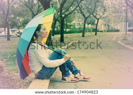 Young woman looks at the sun under a big rainbow umbrella