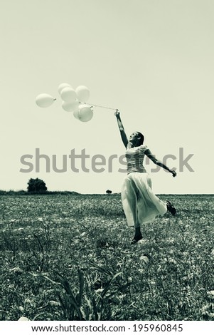Young woman holding pink balloons and flying over a meadow. Photo in old color image style.