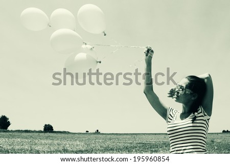 Young woman holding pink balloons and flying over a meadow. Photo in old color image style.