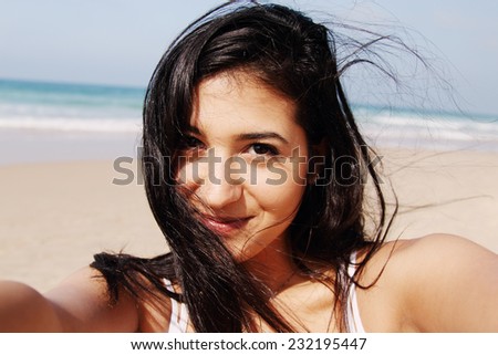 Beautiful girl smiling on the beach with the sand, sea and blue sky in the background. Selfie.