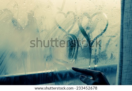 woman drawing heart on wet window