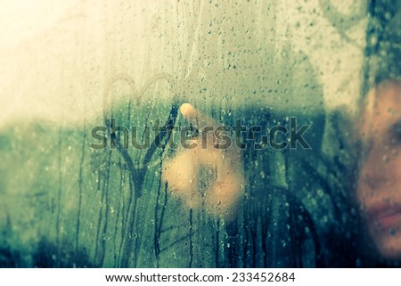 woman drawing heart on wet window