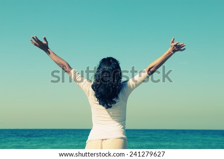 young woman looking up with open arms over sky background