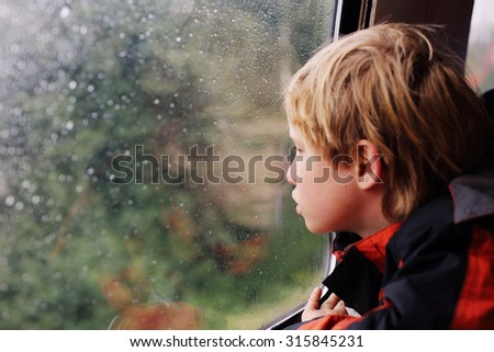 7 years old boy sitting in the train and looking to the rain