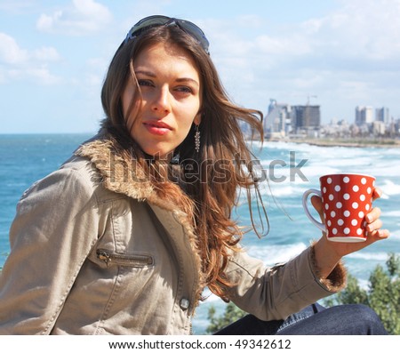 A young girl uses a recess to drink coffee (or tea) near the sea