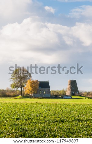 Colorful autumn landscape in the Netherlands with a house, trees and a capless windmill in the background.