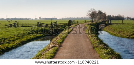 Rural polder landscape with a country road between two ditches and pastures with fences. It is autumn in the Netherlands.