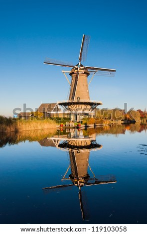Historic windmill in the Netherlands reflected in a mirror smooth water surface of the river.