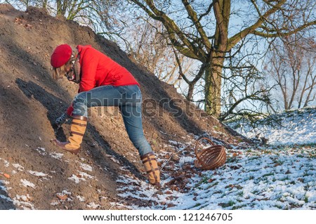Young woman with red cap and coat searching for ancient shards and the like at a mound of earth on a historical site.