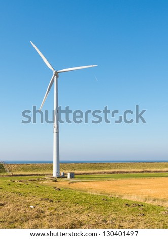 Colorful rural landscape in the Netherlands with a wind turbine against the blue sky.