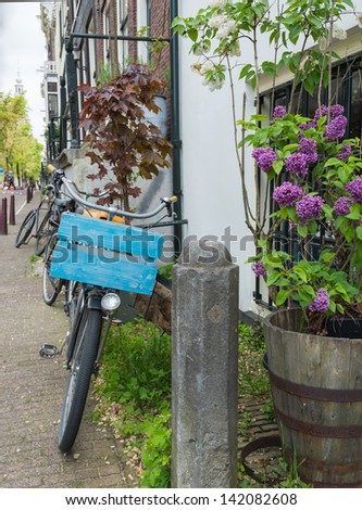 Closeup of an old house with a parked delivery bike, a purple flowering lilac in a tub and a concrete street pole.
